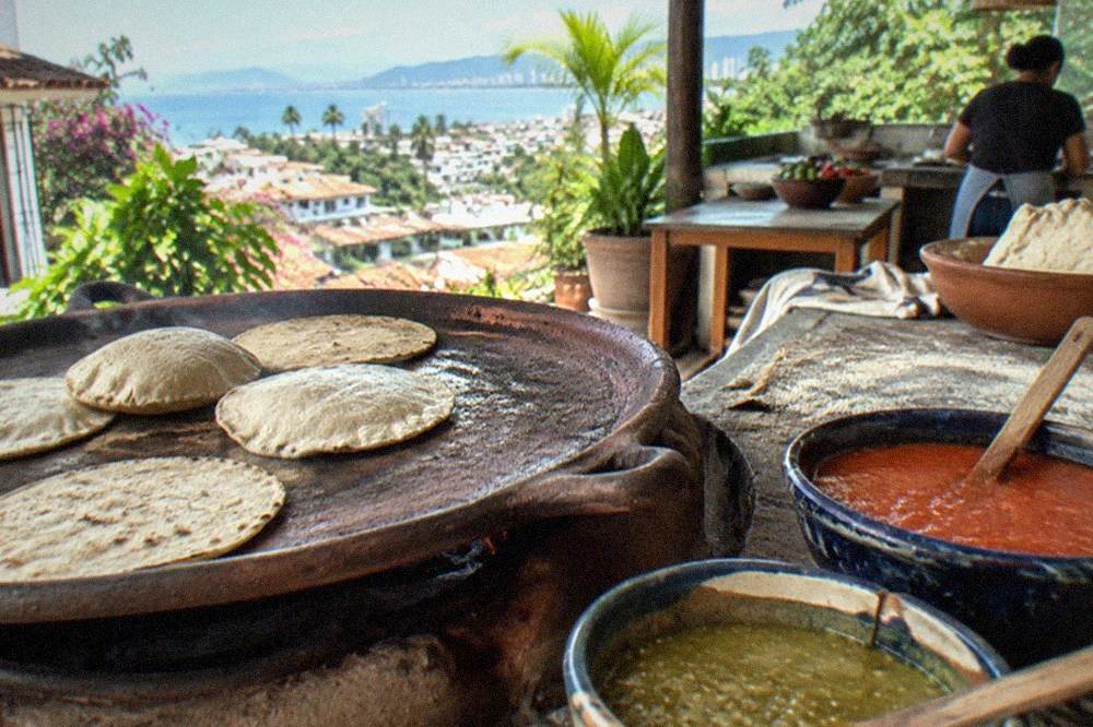 Corn tortillas warming on a clay comal beside bowls of red and green salsa