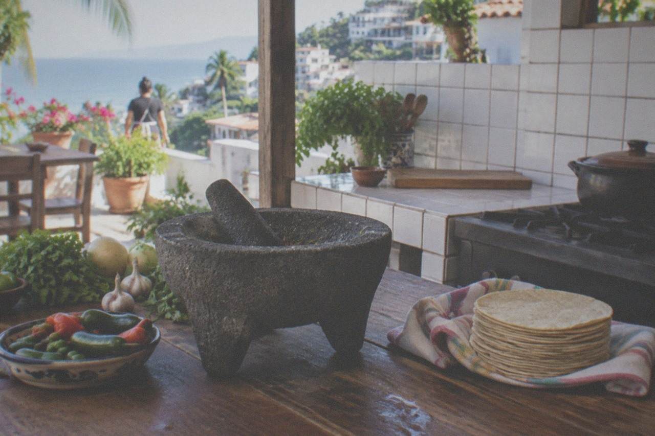 A Mexican cooking counter with a molcajete, fresh chiles, and a stack of corn tortillas