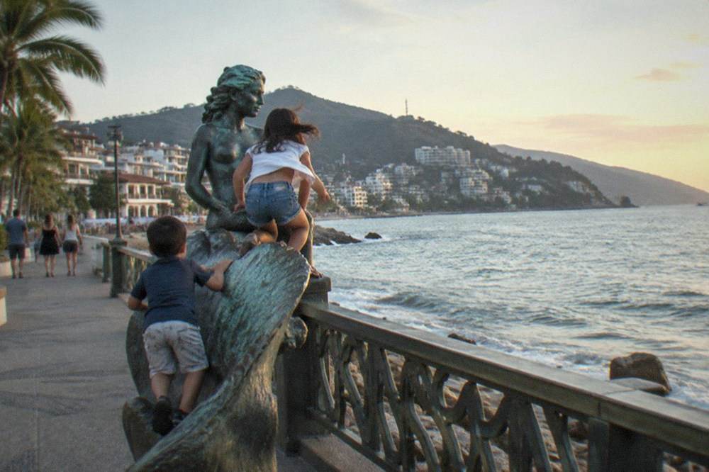 Bronze sculptures lined along the seaside promenade with the bay and distant headland behind them
