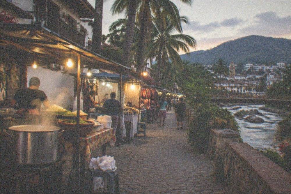 Evening street food stalls with warm lighting along a cobblestone street near the waterfront