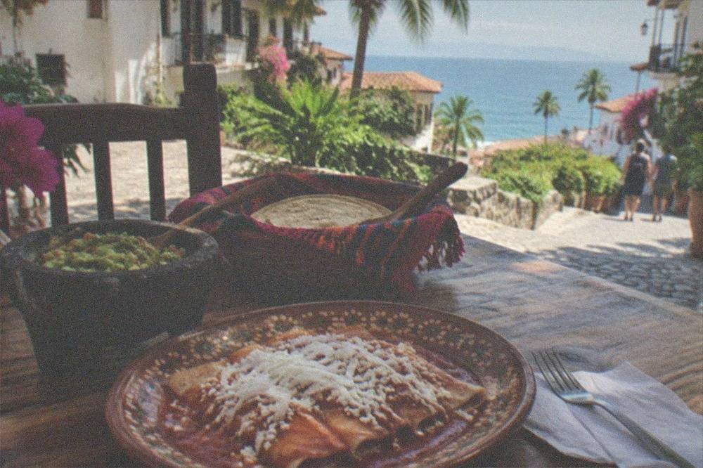 A finished Mexican meal of enchiladas, guacamole, and tortillas plated on a rustic wooden table