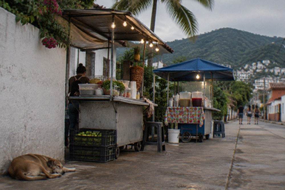 A quiet residential street corner in Puerto Vallarta with small food stands and string lights