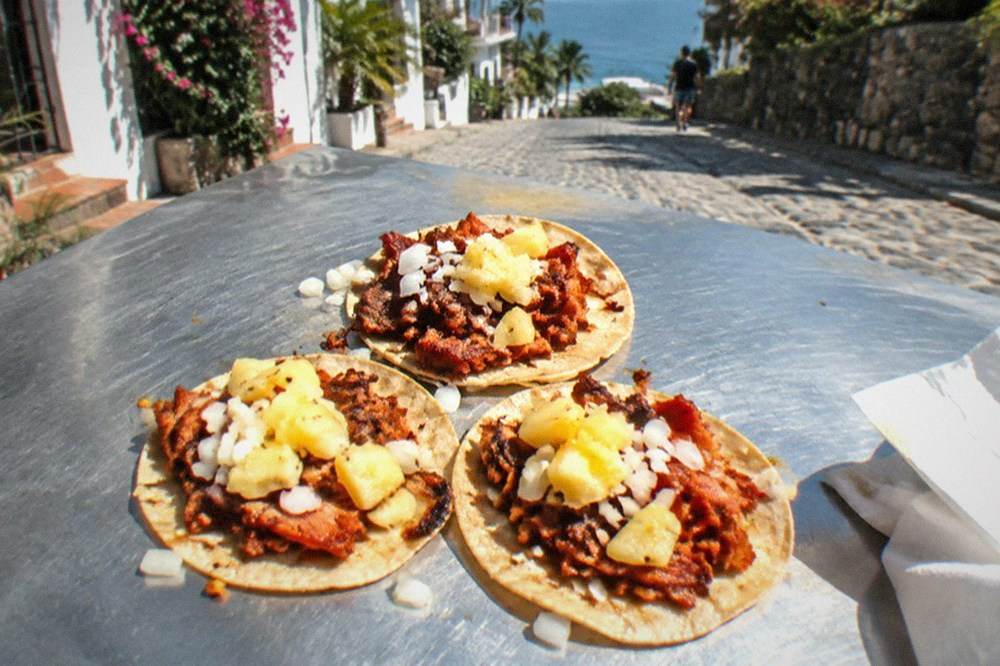 Close-up of tacos al pastor with pineapple, cilantro, and onion on corn tortillas