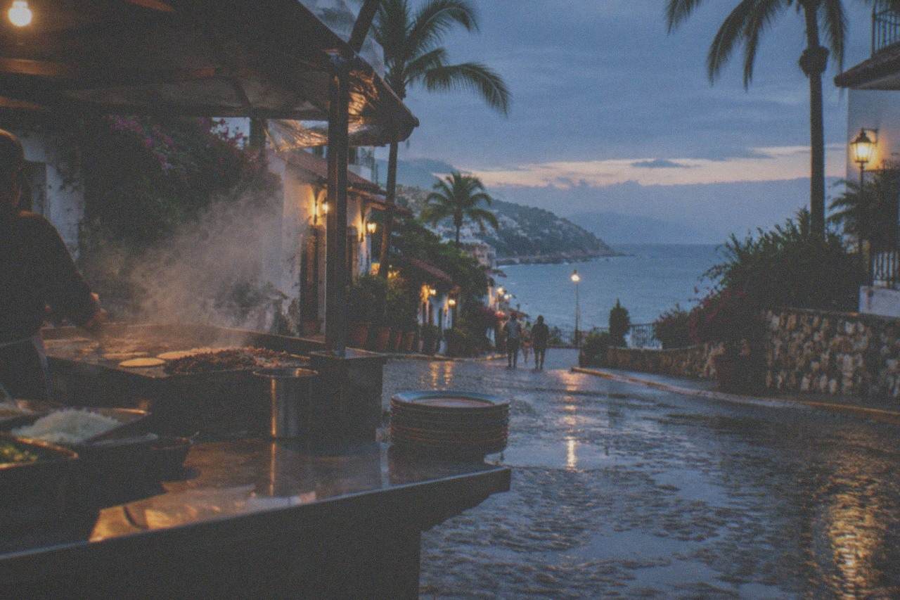 A taco stand at dusk with steam rising from a griddle in a Puerto Vallarta street