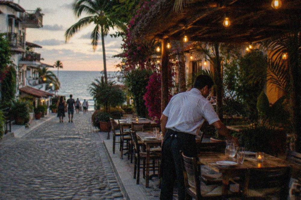 Evening view of a busy restaurant street with outdoor tables and warm lighting
