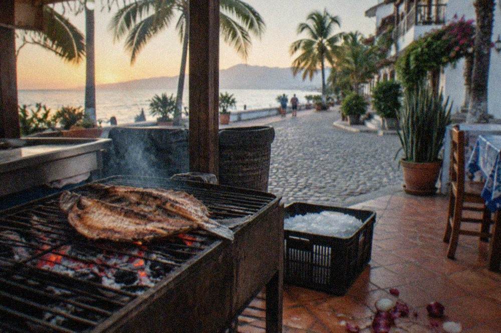 Whole butterflied fish grilling over charcoal at an outdoor seaside restaurant