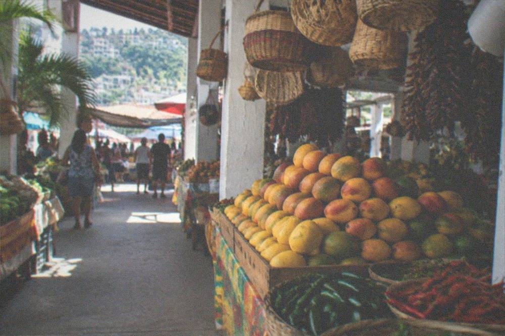 Open air market stalls with fresh produce and hanging baskets above a walkway