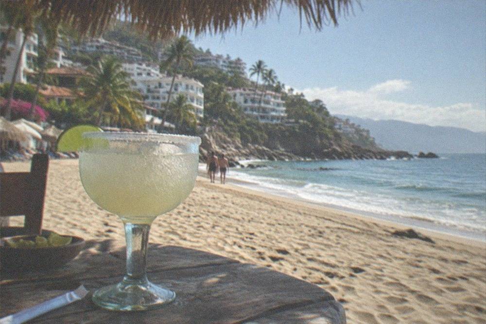 A frosty margarita glass with lime wedges on a sunny beachside table