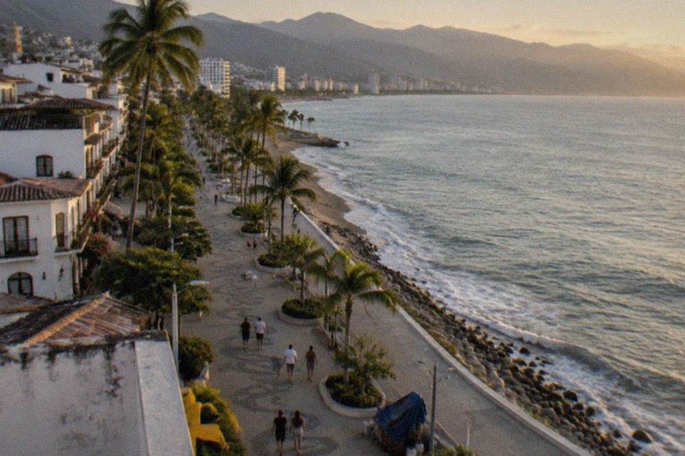 Long straight pedestrian boardwalk along the shoreline with mountains rising behind the city
