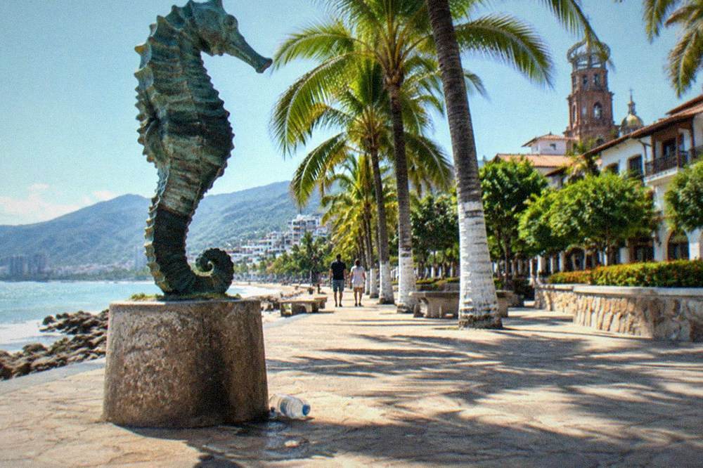 Oceanfront promenade with modern bronze sculptures and palm trees along the paving