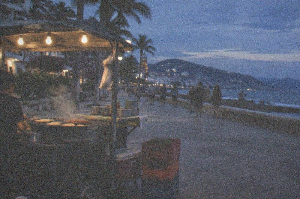 Evening street scene near the waterfront with food stall lights and people strolling
