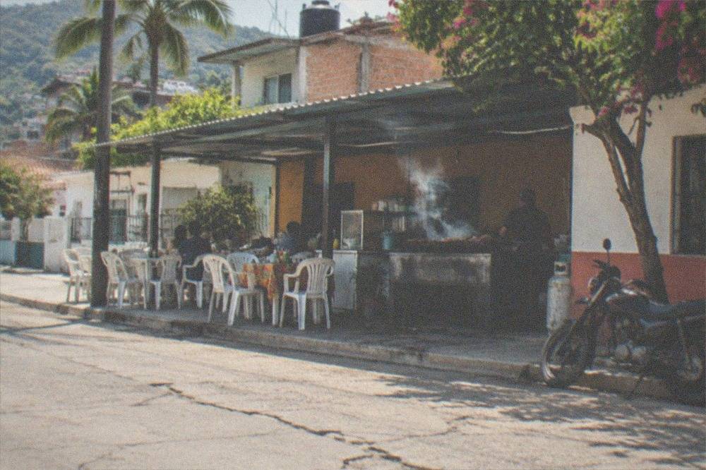 Small neighborhood eatery with plastic chairs and a steaming grill at midday