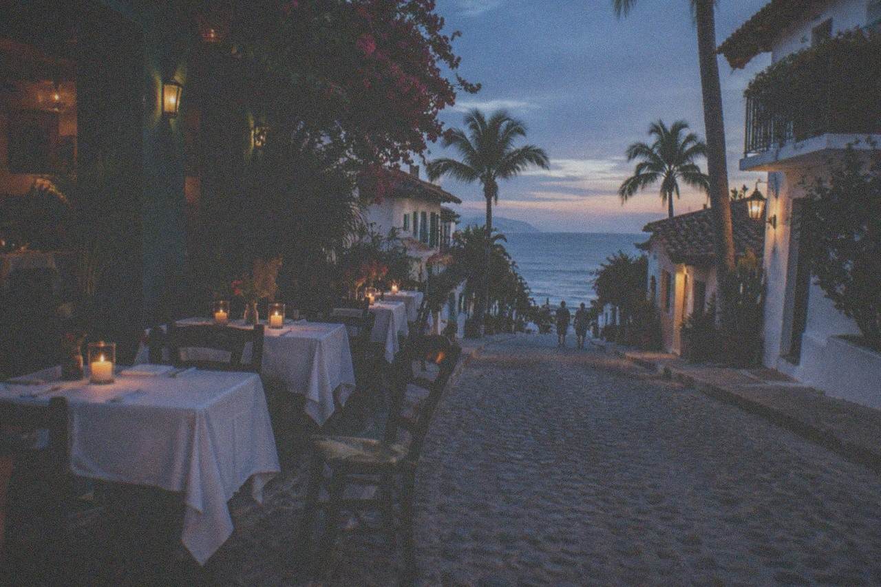 Open-air restaurant tables beside a cobblestone street in Puerto Vallarta at dusk
