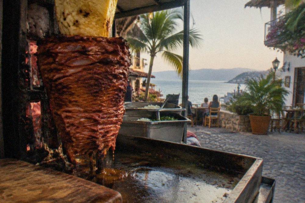 Al pastor trompo spinning beside stacked marinated pork and pineapple at a taco stand
