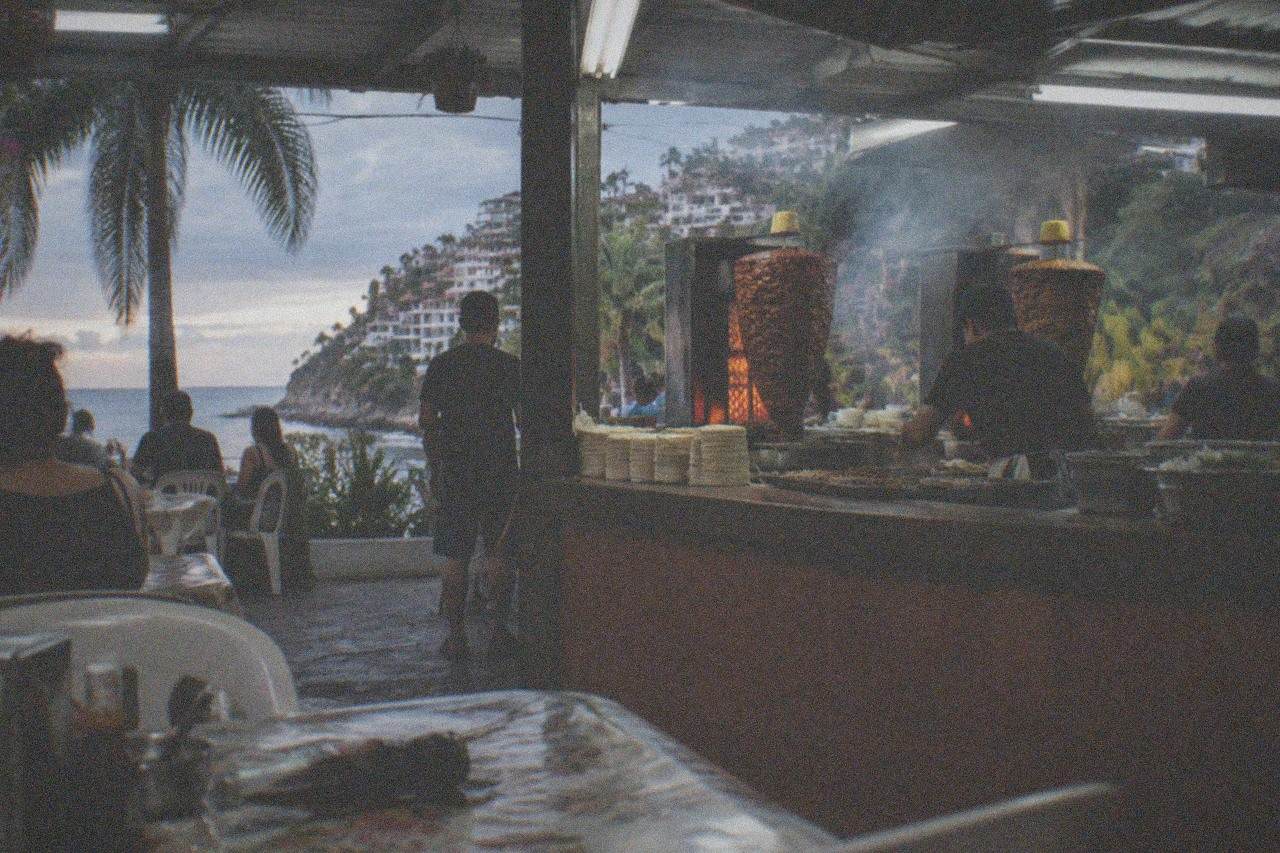 A busy Puerto Vallarta taqueria counter at dusk with trompo spits and stacked tortillas