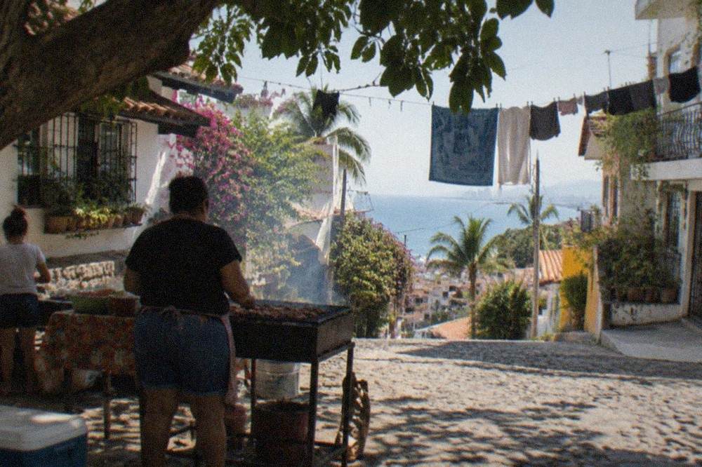 A family-run taco stand grilling meat over charcoal on a residential Puerto Vallarta street corner