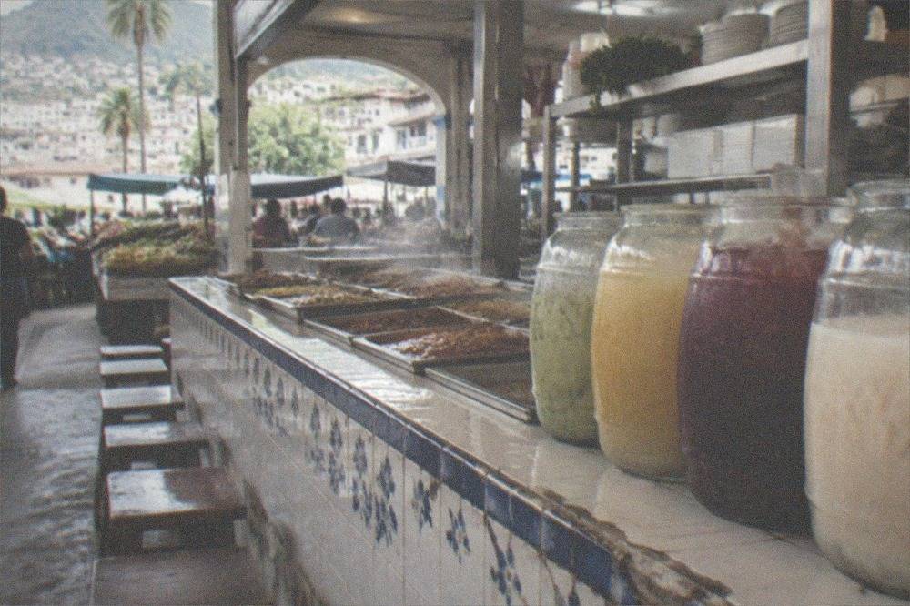 An inexpensive neighborhood fonda counter with steam trays of stews and a row of aguas frescas in jars