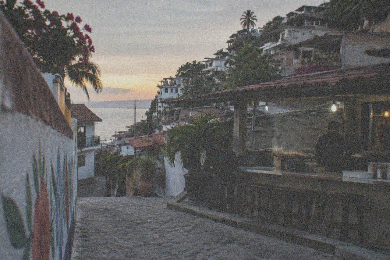A small neighborhood taqueria counter in Puerto Vallarta at dusk with steam rising from a grill
