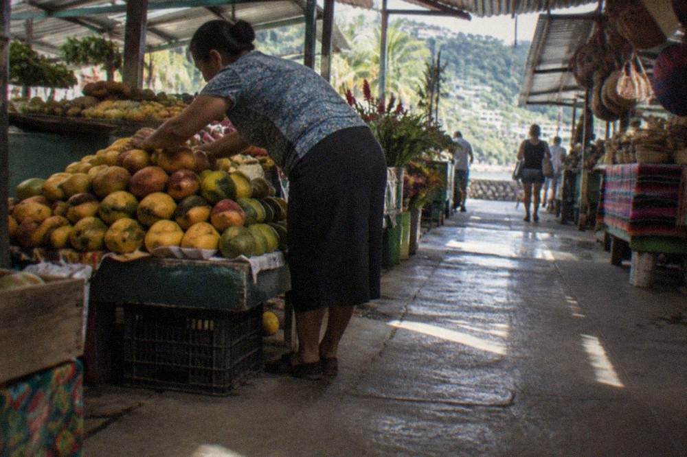 Interior market aisle with produce stalls and vendors arranging fruit under warm lighting