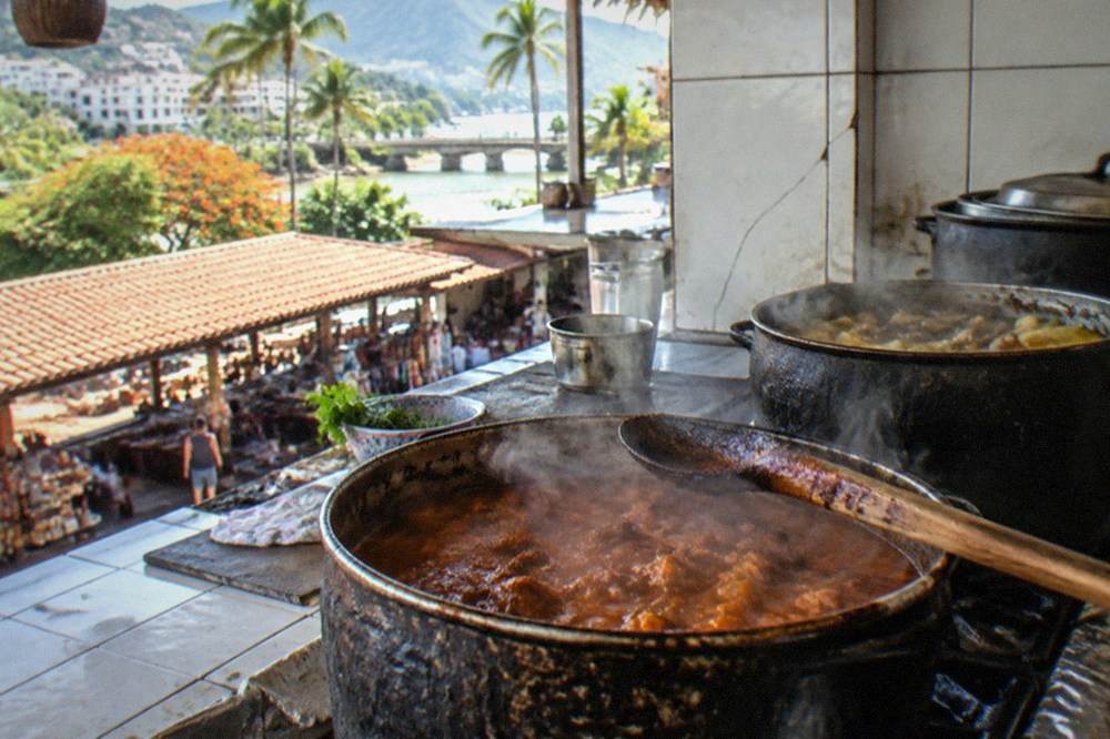 Steam rising from pots of stew at a small market food counter with tiled surfaces