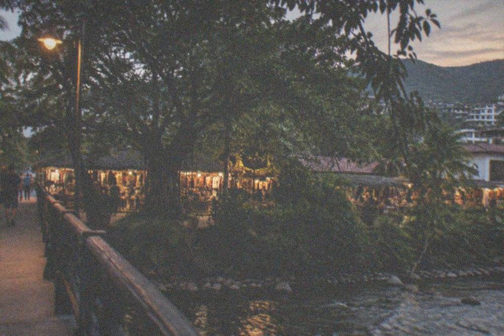 Pedestrian footbridge over a river toward a tree-covered island with market buildings