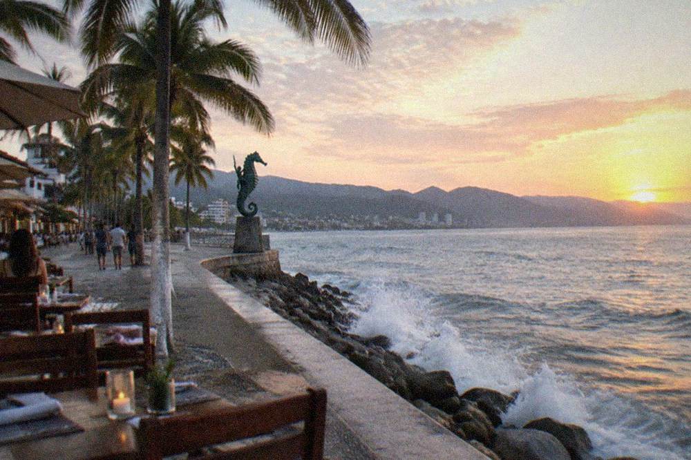 Oceanfront boardwalk restaurant tables at dusk with the Malecon walkway and palm trees