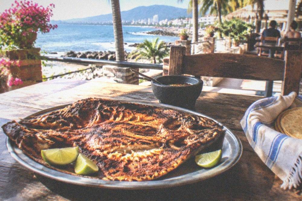 Whole butterflied grilled fish served with lime wedges and tortillas on a rustic plate
