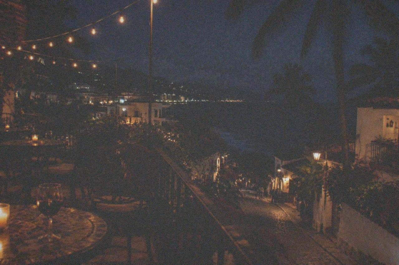 Evening view of a candlelit restaurant terrace with string lights above cobblestone street tables