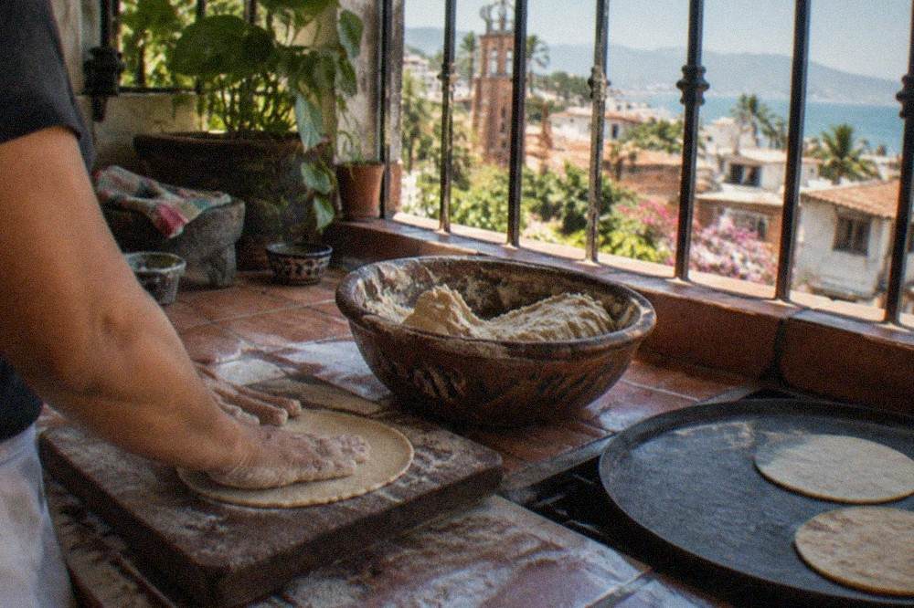 A cook pressing fresh corn tortillas by hand on a rustic kitchen counter beside a bowl of masa
