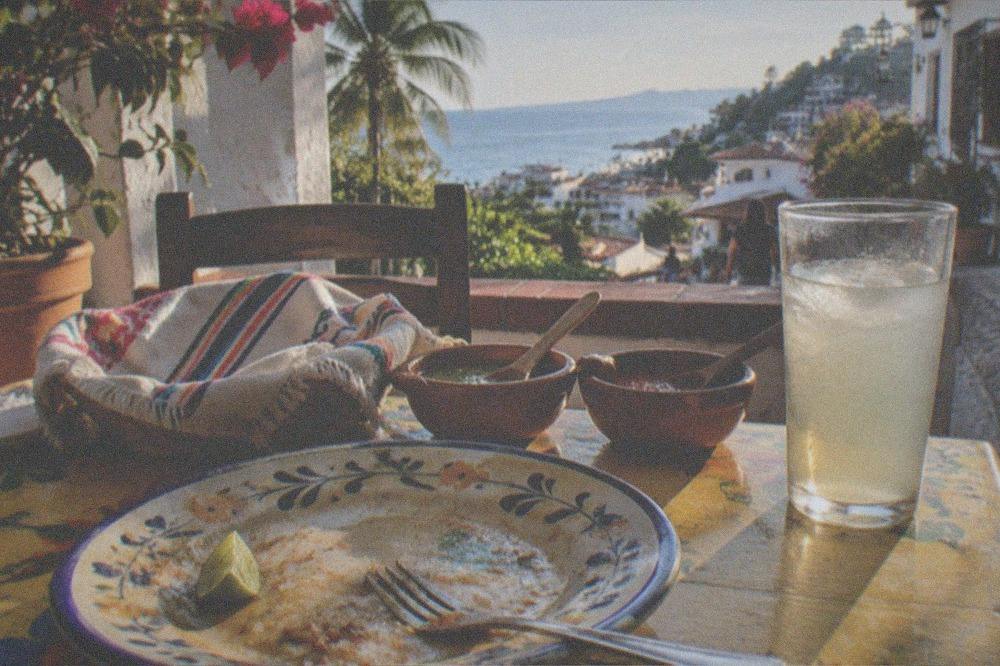 A finished Mexican meal plated on a colorful table with salsas, tortillas and a glass of agua fresca