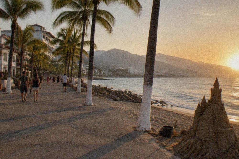 Wide pedestrian boardwalk along the ocean with palm trees and distant mountains at golden hour