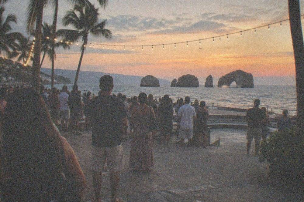Open-air amphitheater stage by the ocean with an evening crowd gathered under string lights
