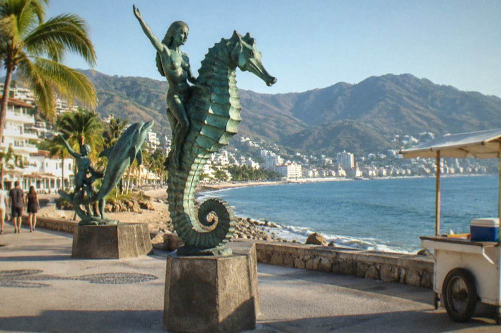 Bronze sculptures along the seaside promenade with the bay and hills behind them