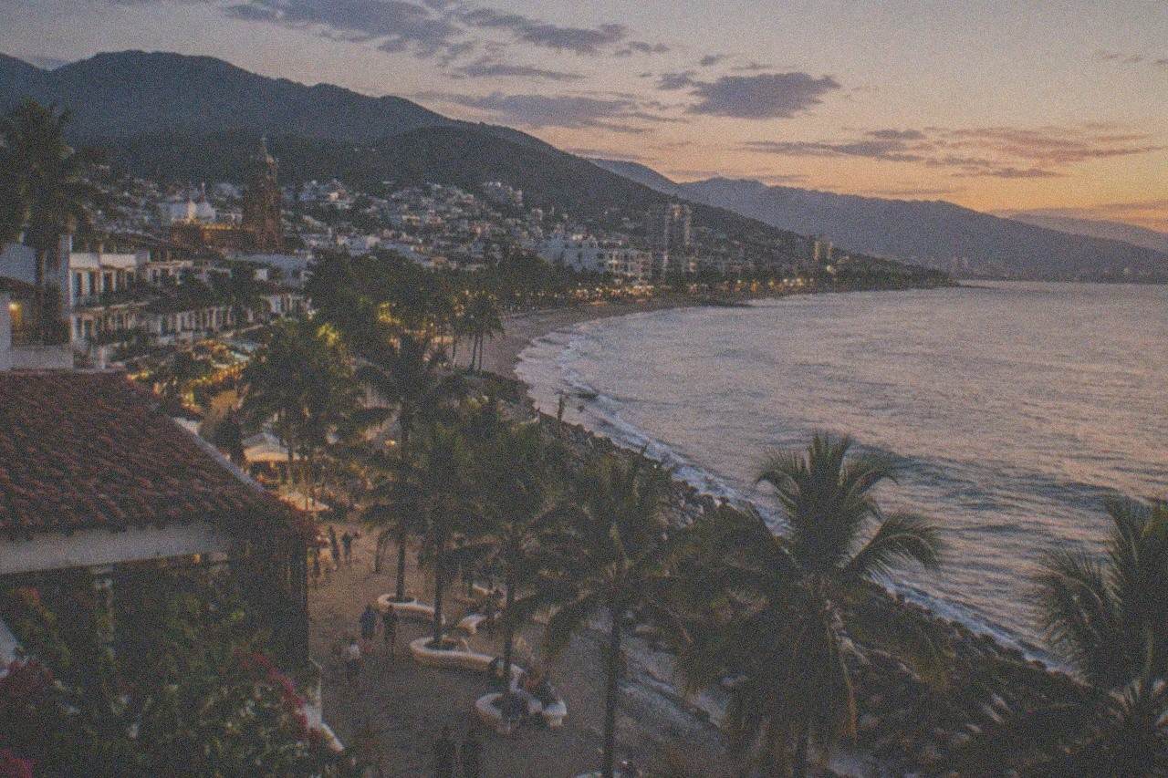 Oceanfront boardwalk with palm trees, sculptures and the Puerto Vallarta skyline at dusk