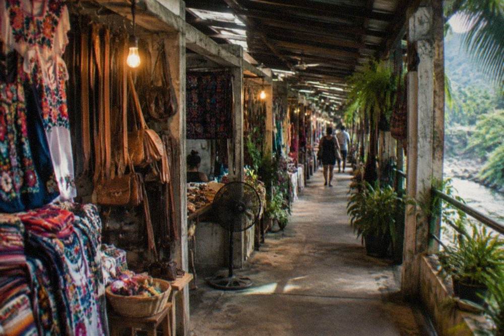 Covered market aisle with hanging woven bags and colorful crafts under warm lighting