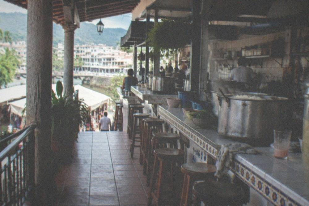Second-floor food counter with steaming pots and a row of stools facing the kitchen