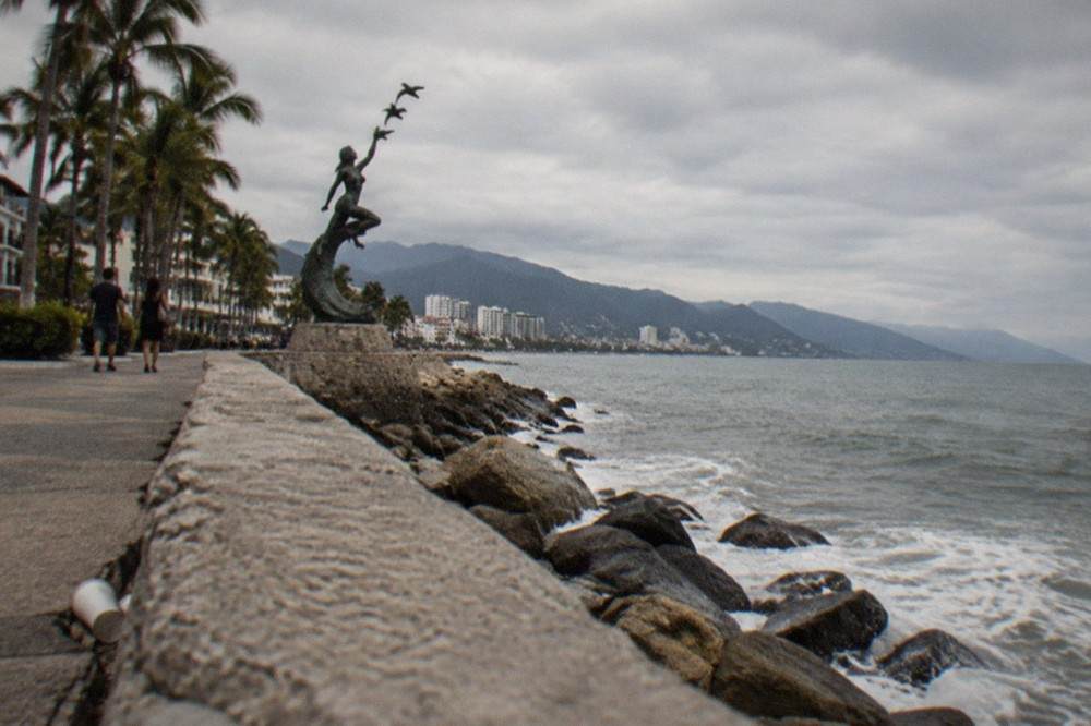 Oceanfront boardwalk in Puerto Vallarta with palm trees and sculptures along the water