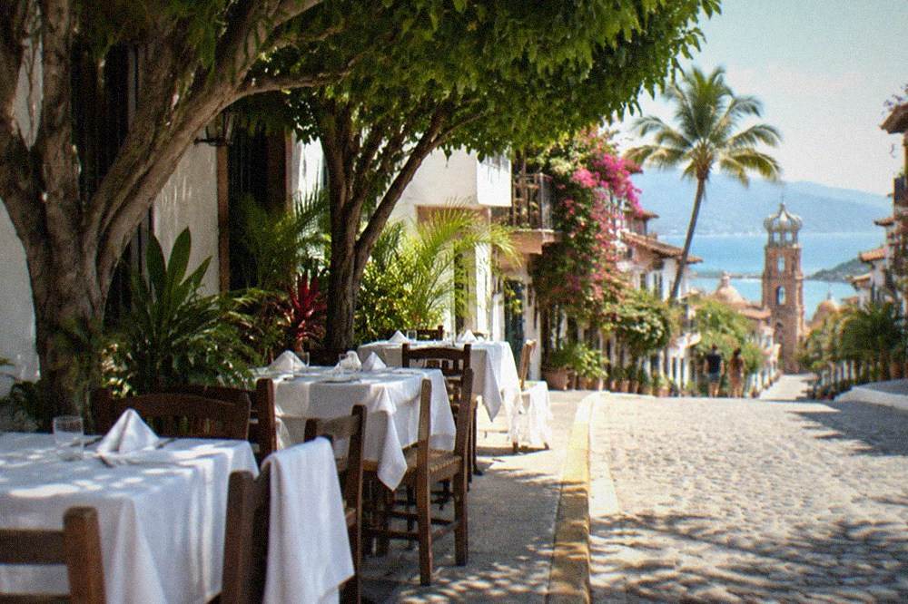 Restaurant tables with white tablecloths set along a tree-lined Old Town street in Puerto Vallarta