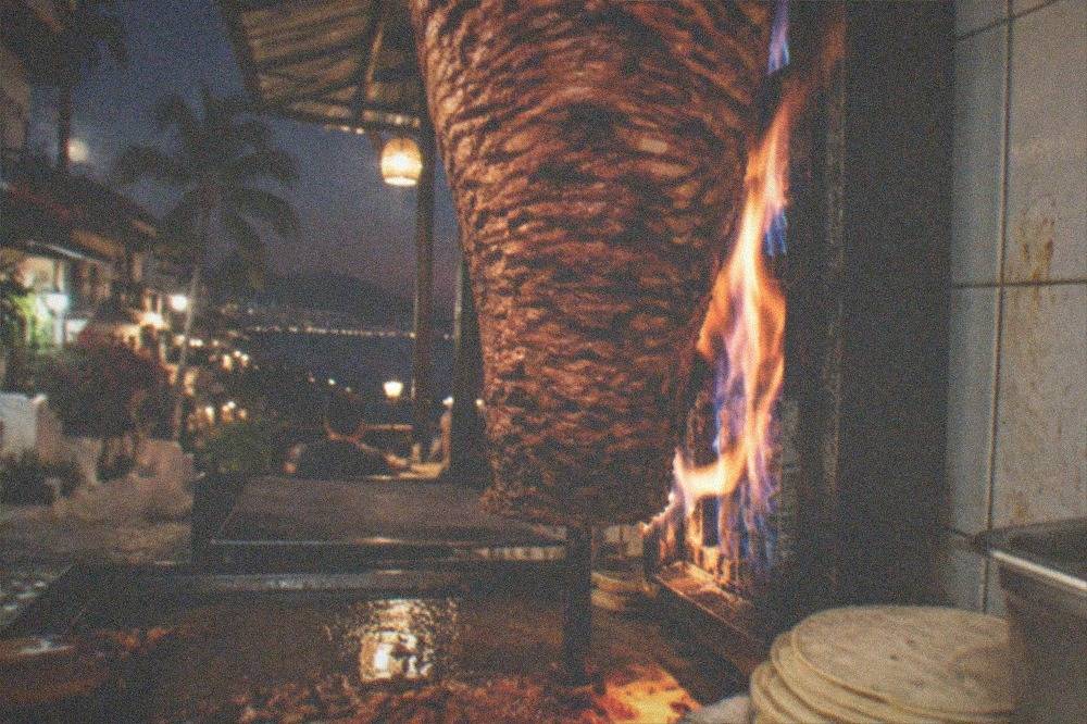 Close view of al pastor tacos being sliced from a vertical spit at a busy Old Town taqueria counter