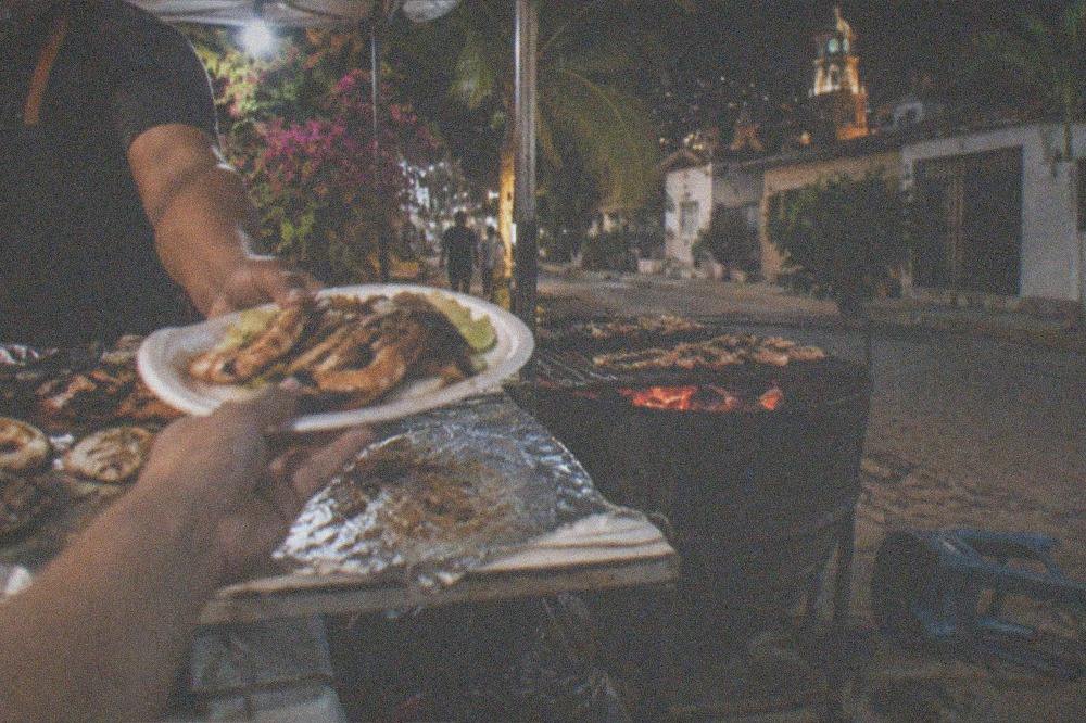 Evening food stall with grilled seafood plates being handed across a counter