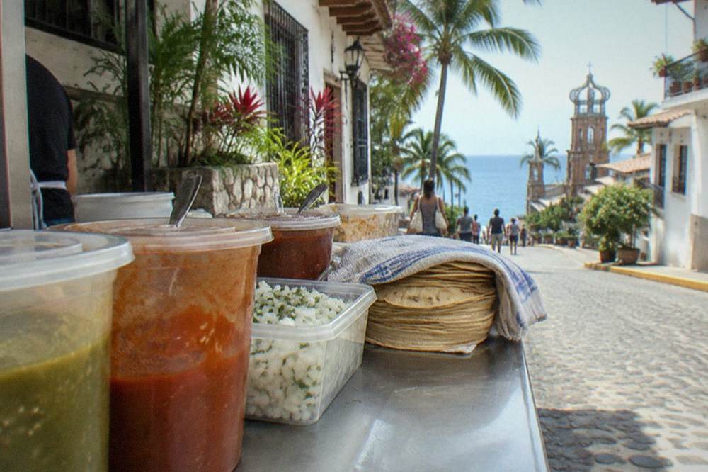 A row of covered salsa containers and fresh ingredients at a busy taco stand counter