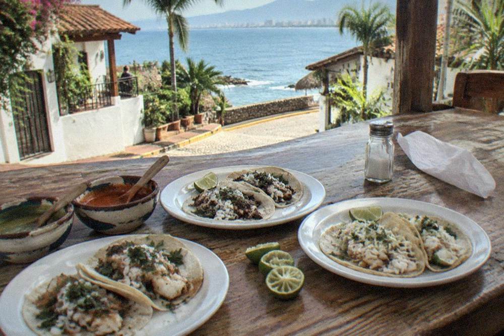 Plates of tacos arranged on a wooden counter with lime wedges and salsas