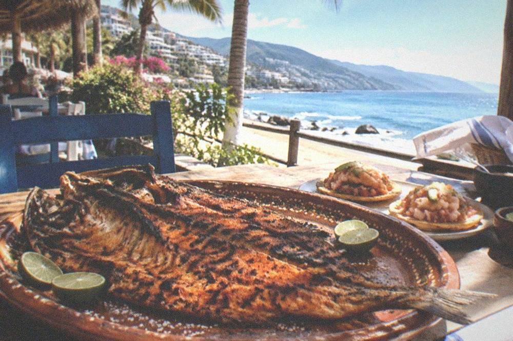 Whole grilled fish and shrimp tostadas served on a beachside table