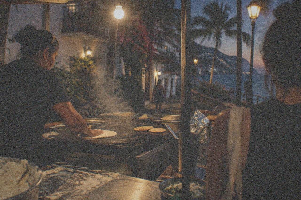 Street taco stand at night with a cook pressing tortillas by hand