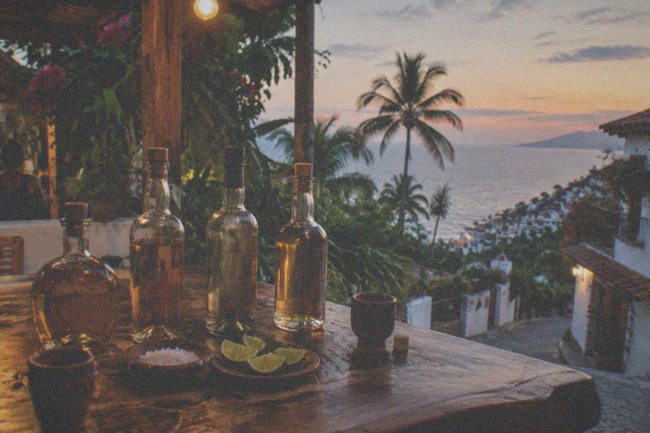 Bottles of tequila and mezcal arranged on a rustic wooden bar counter with lime wedges and salt