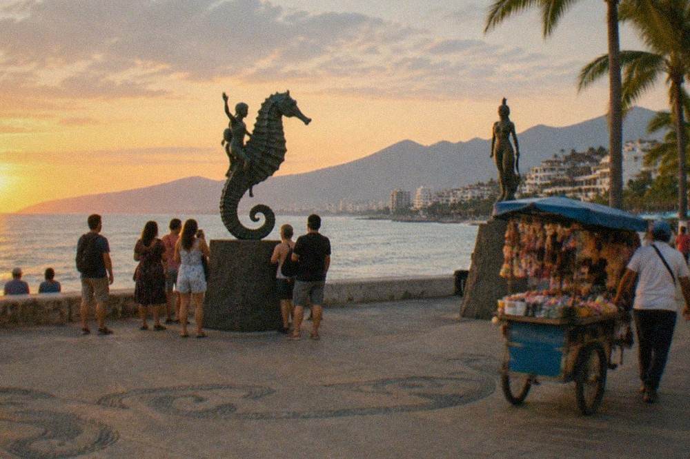 Oceanfront boardwalk with palm trees, sculptures and the bay beyond at golden hour