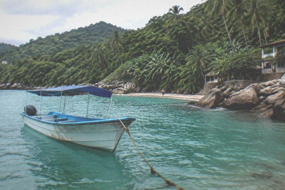 Small boat anchored in a cove with dense green jungle hills rising behind a sandy shoreline