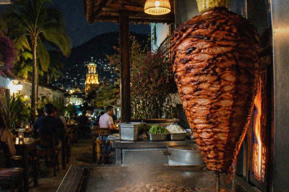 Vertical al pastor spit with stacked marinated pork and a pineapple on top inside a taqueria