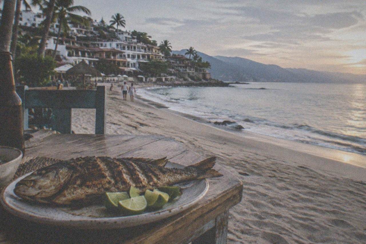 Grilled snapper and lime wedges on a beachfront table beside the ocean